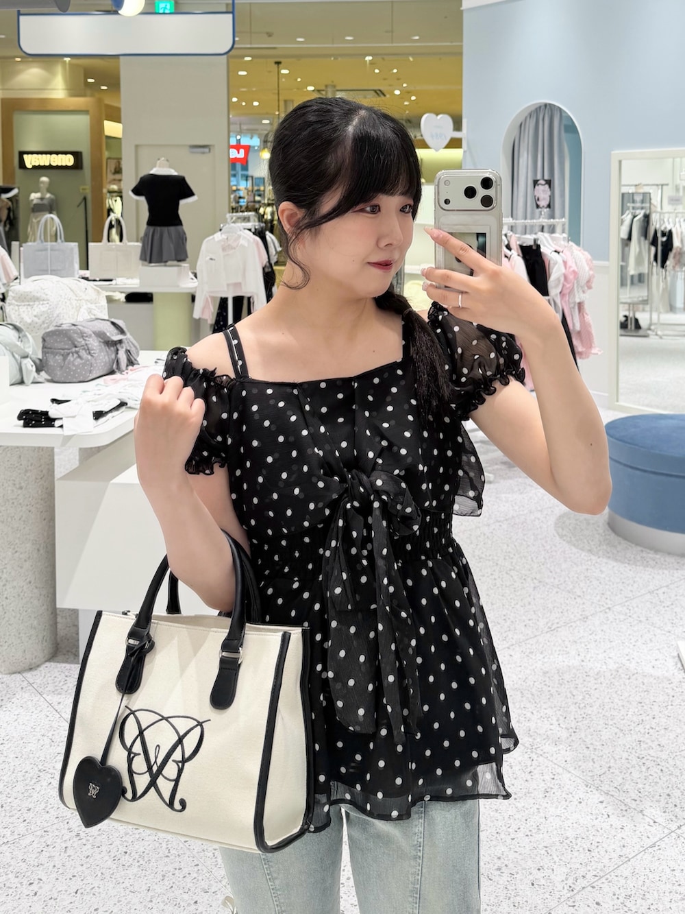 ブラック系のチュニック、ブルー系のデニムパンツ、ホワイト系のトートバッグを着用したレディースの春コーディネートの2枚目の写真