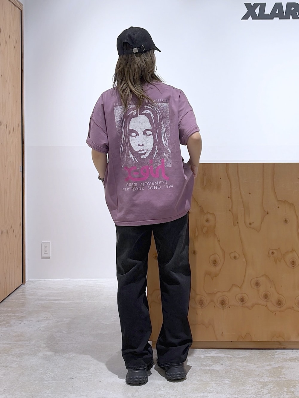 ブラック系のデニムパンツ、パープル系のワンピース、ブラック系のキャップを着用したレディースの春コーディネートの2枚目の写真