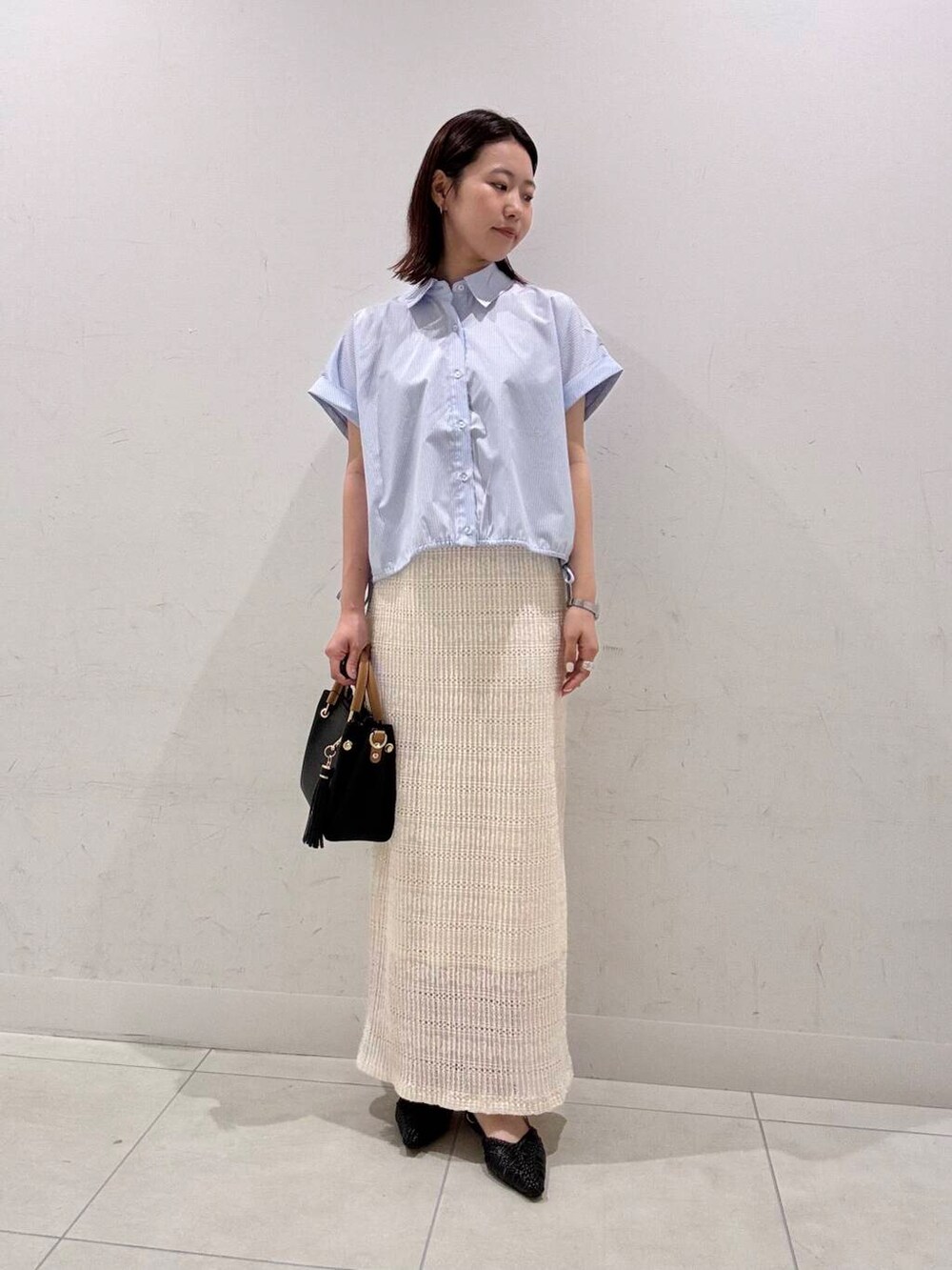 ブラック系のトートバッグ、ブラック系のサンダル、ホワイト系のスカートを着用したレディースの春コーディネートの2枚目の写真