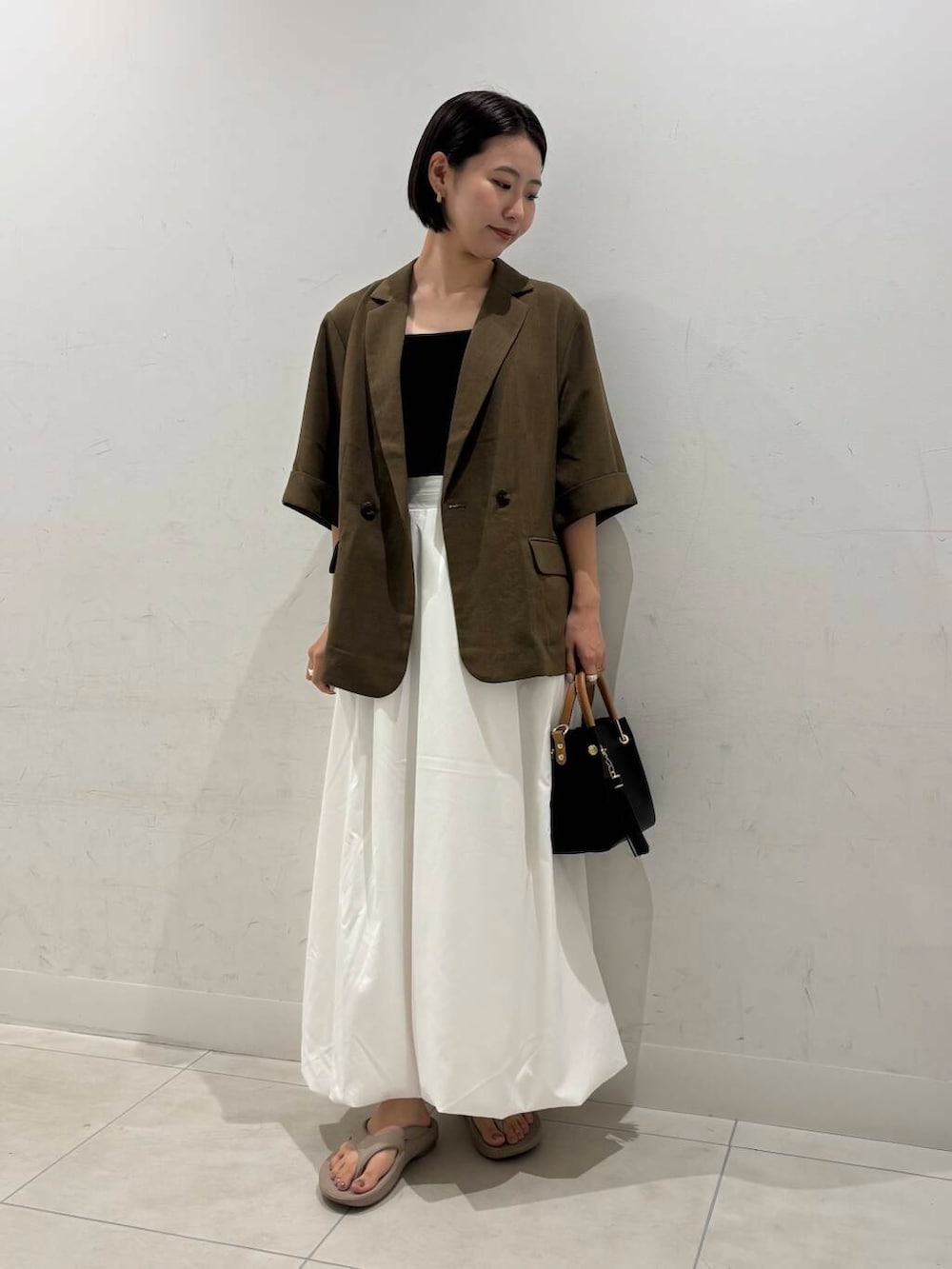 ブラック系のトートバッグ、ホワイト系のスカート、ベージュ系のサンダルを着用したレディースの夏コーディネートの3枚目の写真