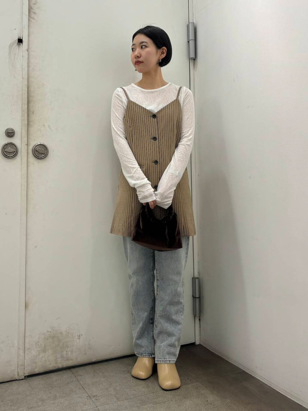 ブルー系のデニムパンツ、ベージュ系のサンダル、ブラウン系のハンドバッグを着用したレディースの秋コーディネートの2枚目の写真