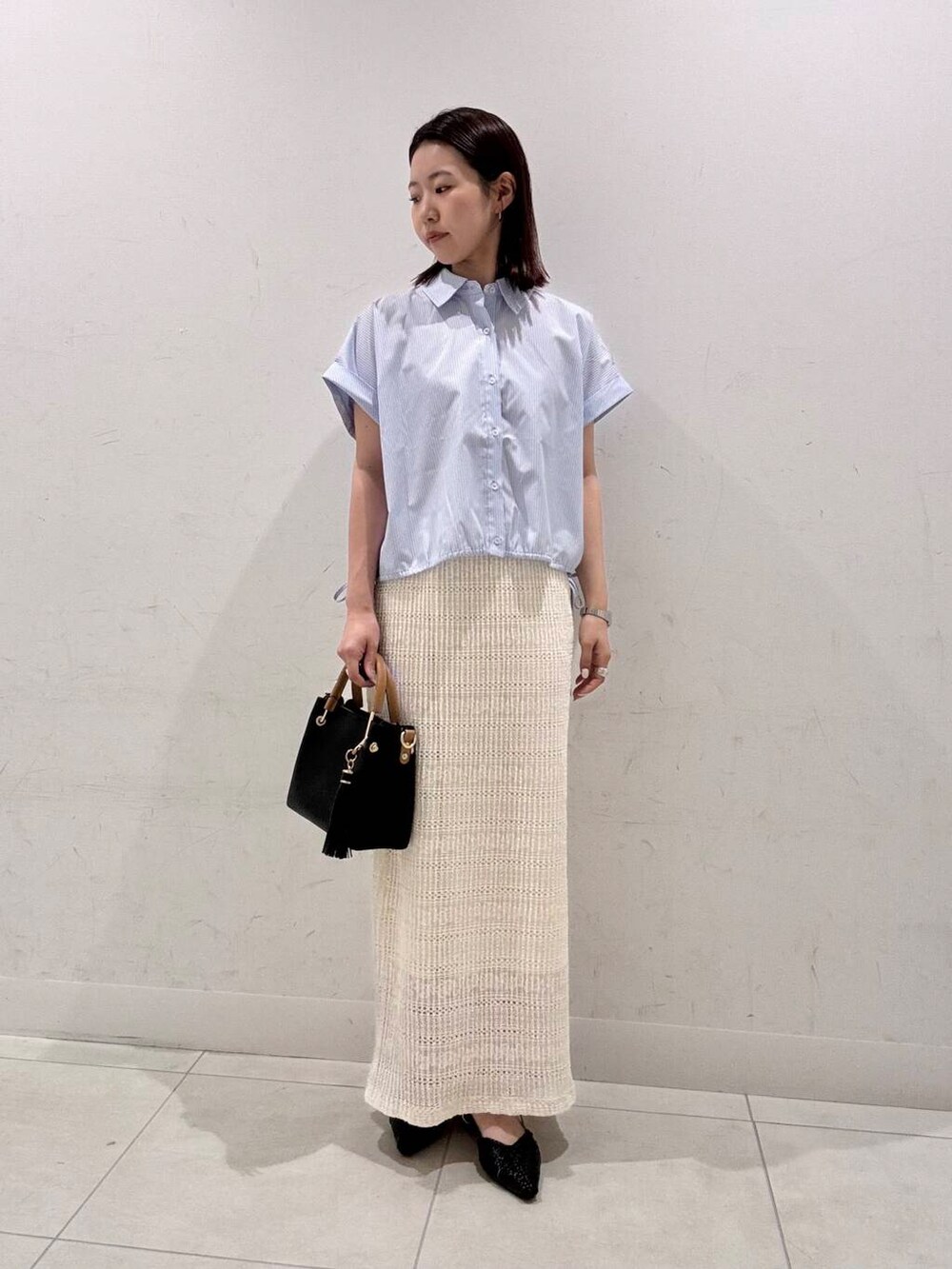 ブラック系のトートバッグ、ブラック系のサンダル、ホワイト系のスカートを着用したレディースの春コーディネートの3枚目の写真