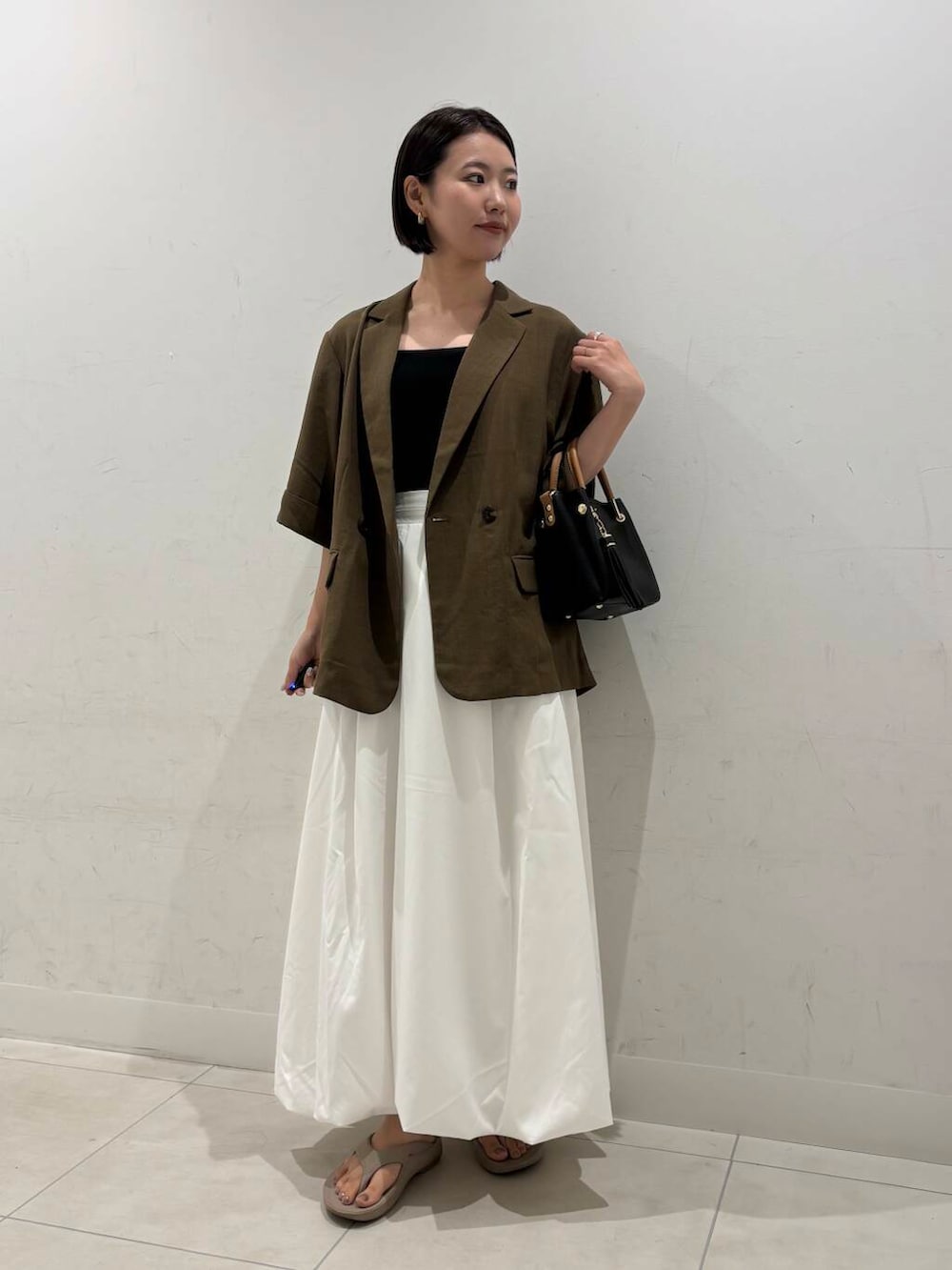 ブラック系のトートバッグ、ホワイト系のスカート、ベージュ系のサンダルを着用したレディースの夏コーディネートの2枚目の写真