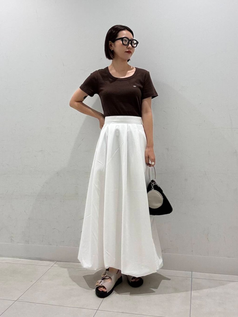 ホワイト系のスカート、ブラック系のハンドバッグ、グレー系のサンダルを着用したレディースの夏コーディネートの2枚目の写真