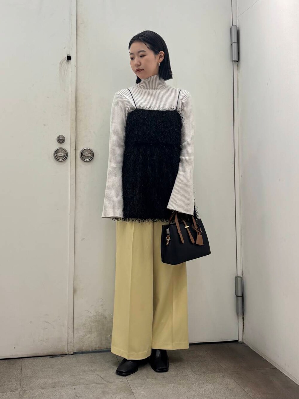 ブラック系のハンドバッグ、ホワイト系のニット/セーター、ブラック系のブーツを着用したレディースの冬コーディネートの2枚目の写真