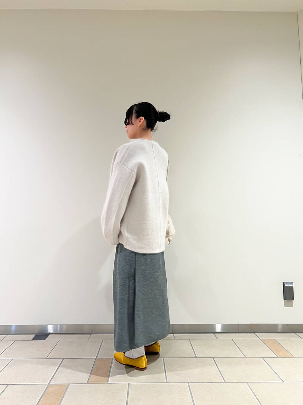 イエロー系のバレエシューズ、グレー系のカーディガン/ボレロ、ホワイト系のショルダーバッグを着用したレディースの冬コーディネートの2枚目の写真