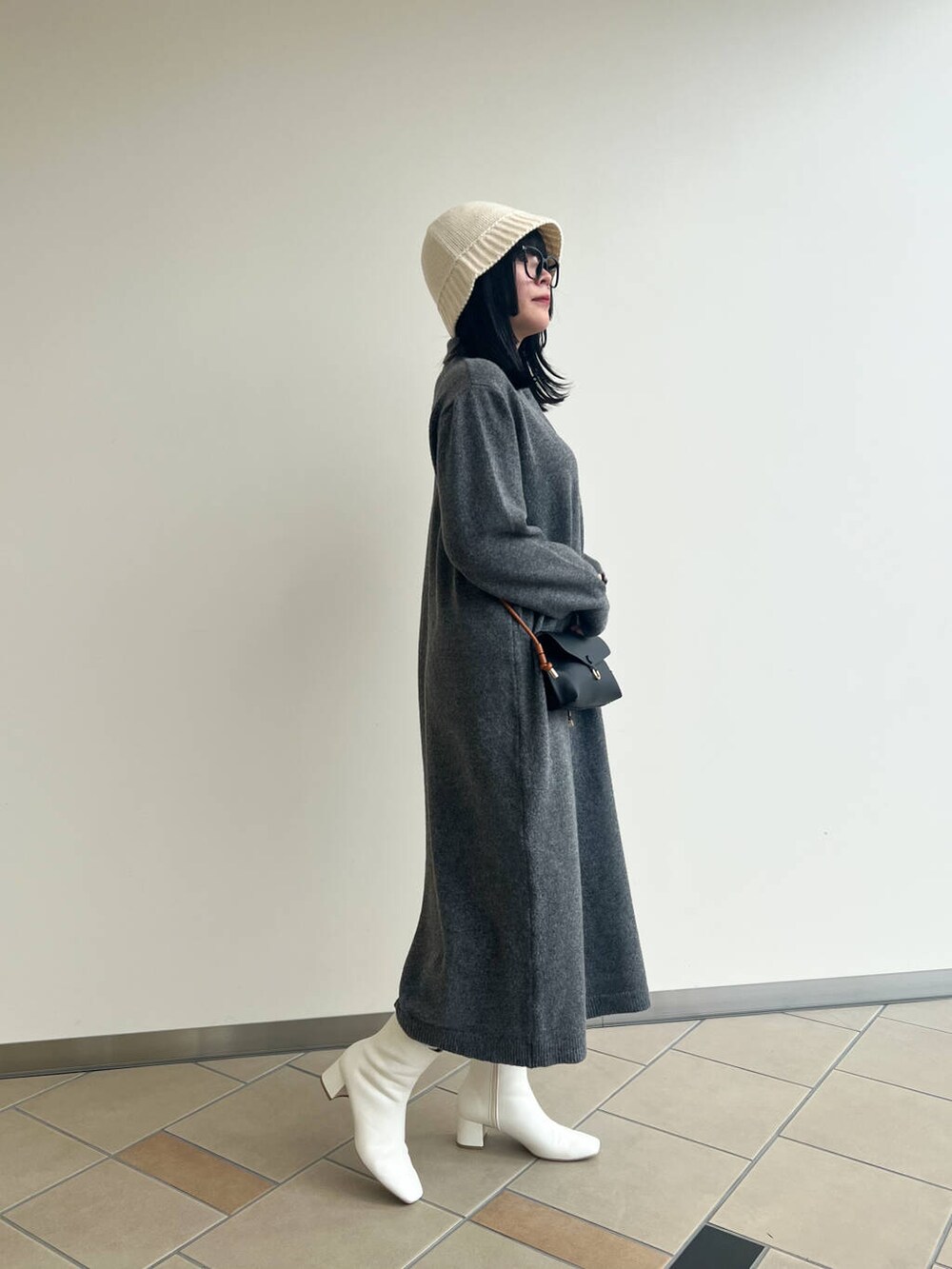 ブラック系のショルダーバッグ、ホワイト系のブーツ、グレー系のワンピースを着用したレディースの秋コーディネートの2枚目の写真