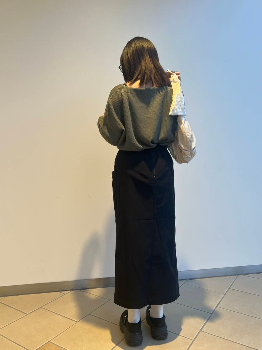 ベージュ系のハンドバッグ、ブラック系のスカート、グリーン系のニット/セーターを着用したレディースの夏コーディネートの2枚目の写真