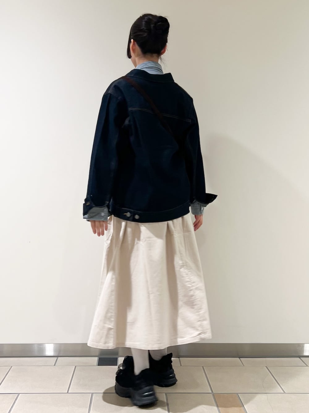 ホワイト系のスカート、ブルー系のデニムジャケット、ブラウン系のショルダーバッグを着用したレディースの秋コーディネートの2枚目の写真