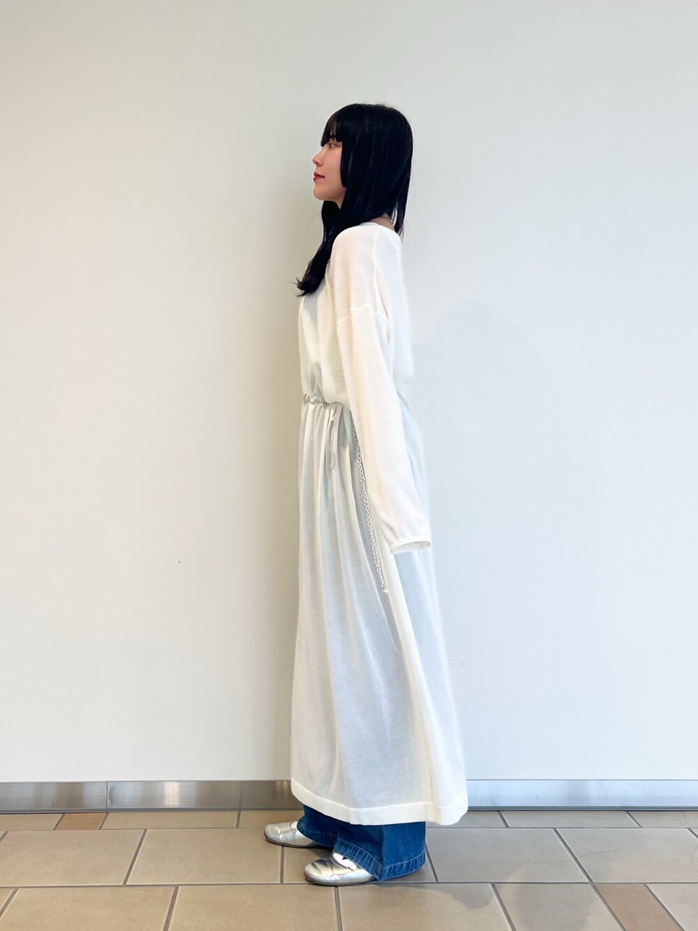 ホワイト系のワンピース、ブラウン系のショルダーバッグ、ブルー系のデニムパンツを着用したレディースの秋コーディネートの2枚目の写真