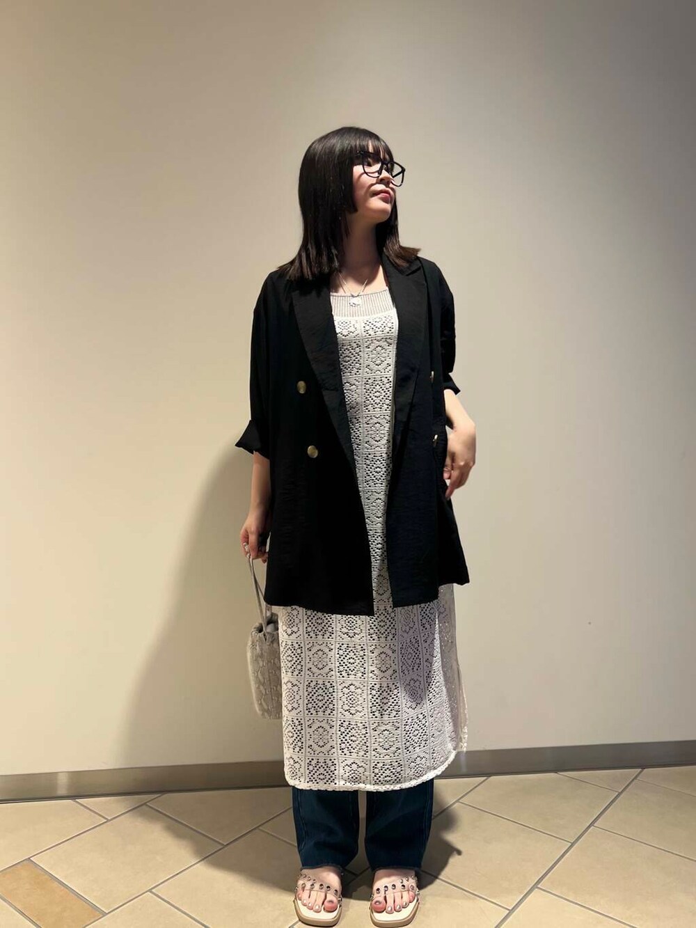 ホワイト系のハンドバッグ、ブラック系のテーラードジャケット、ホワイト系のサンダルを着用したレディースの夏コーディネートの2枚目の写真