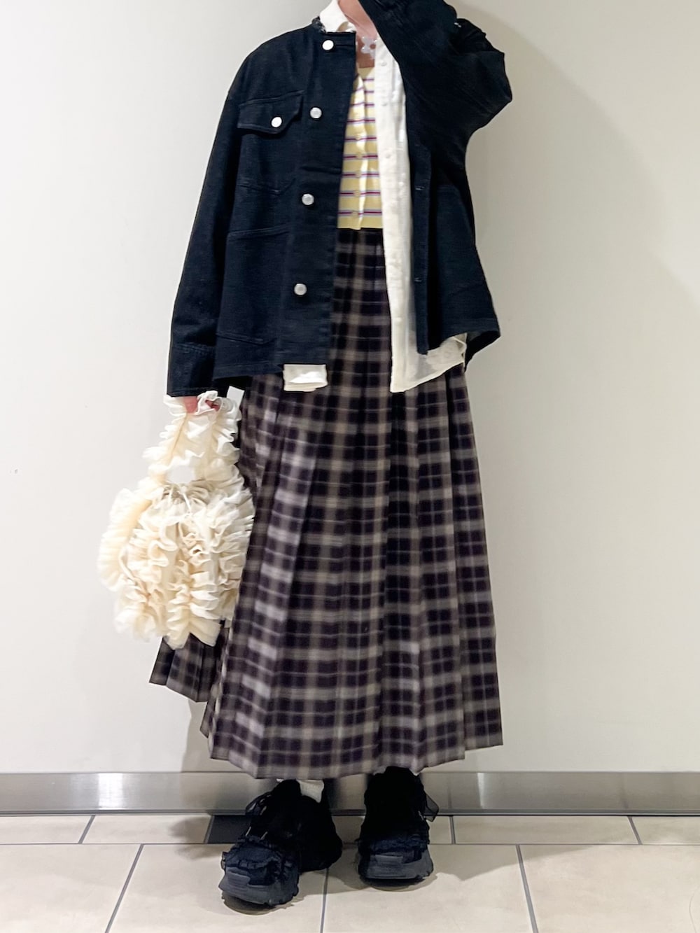 ブラック系のデニムジャケット、イエロー系のニット/セーター、ブルー系のスカートを着用したレディースの春コーディネートの3枚目の写真