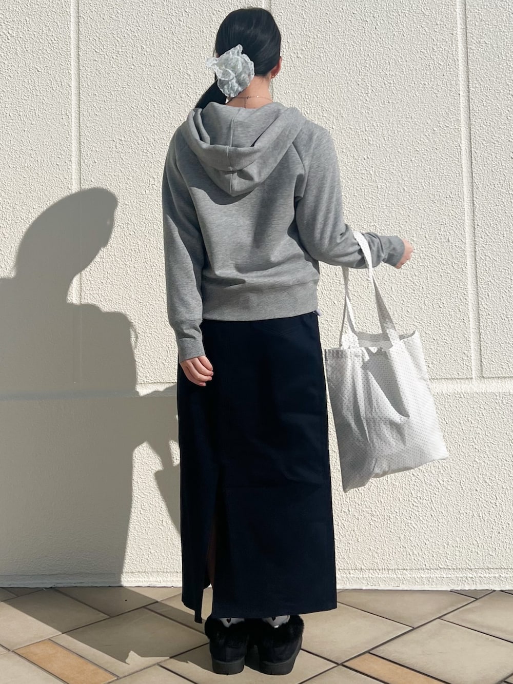ホワイト系のトートバッグ、ブルー系のスカート、グレー系のパーカーを着用したレディースの冬コーディネートの2枚目の写真