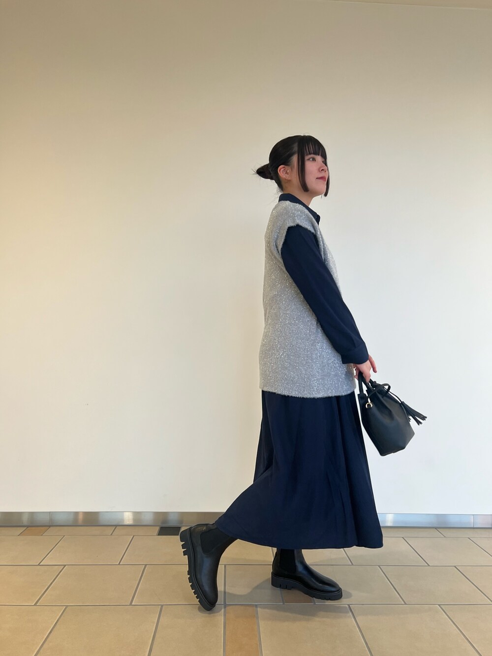 グレー系のベスト、ブルー系のワンピース、ブラック系のショルダーバッグを着用したレディースの秋コーディネートの2枚目の写真