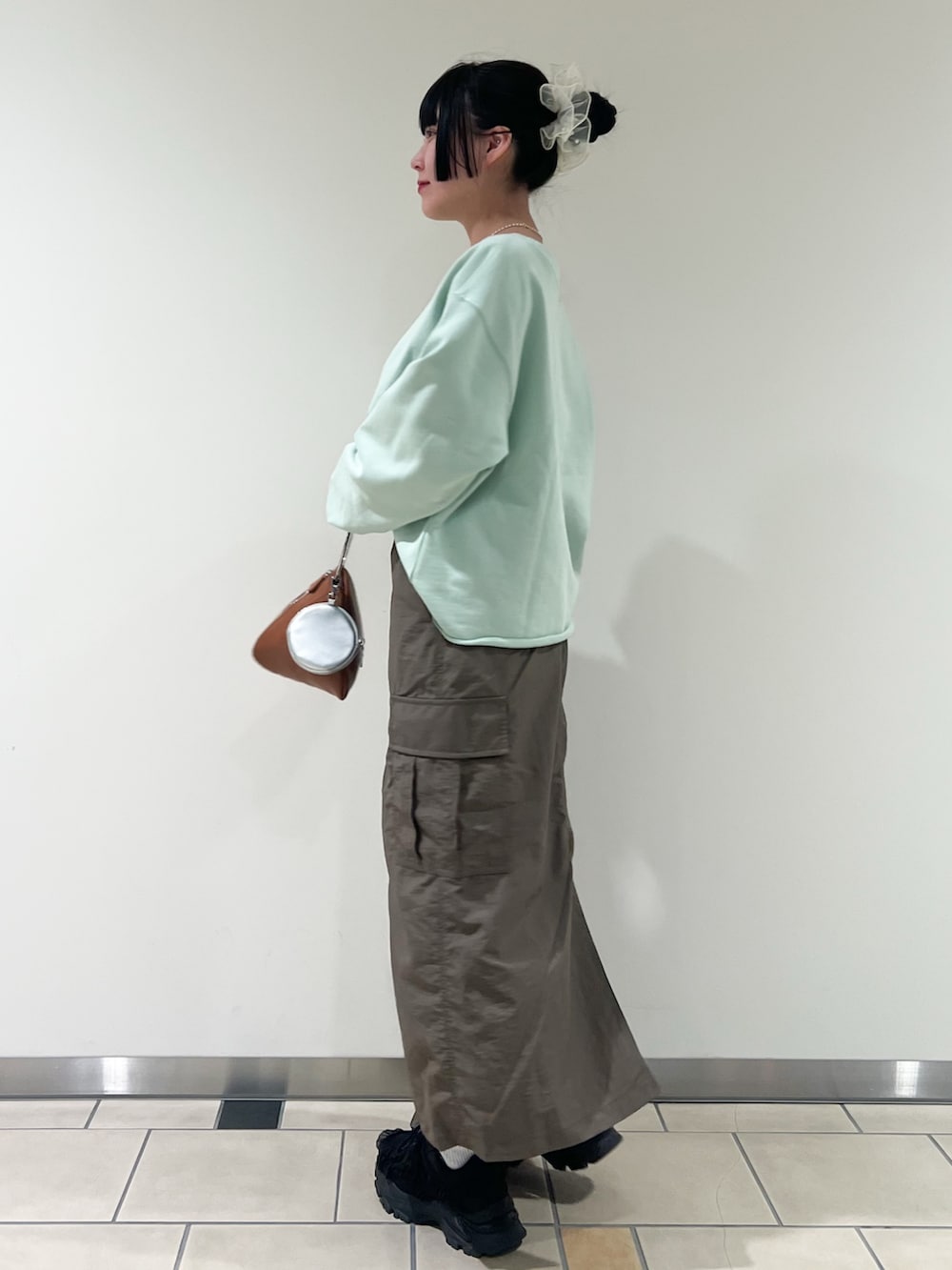 イエロー系のハンドバッグ、グリーン系のスウェット、ホワイト系のネックレスを着用したレディースの春コーディネートの2枚目の写真