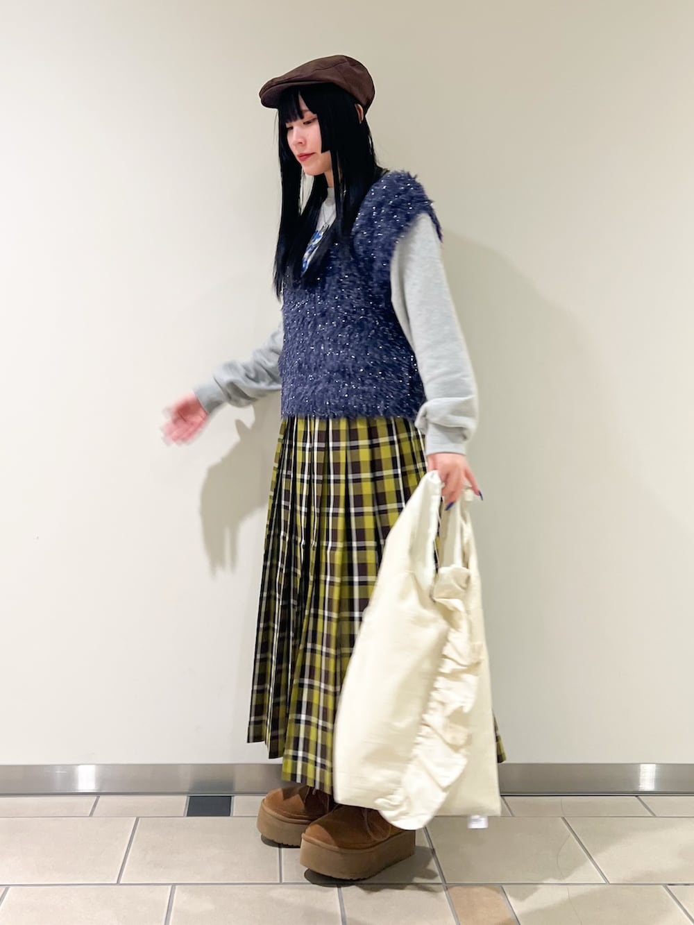 ホワイト系のトートバッグ、グリーン系のスカート、ブルー系のベストを着用したレディースの冬コーディネートの2枚目の写真