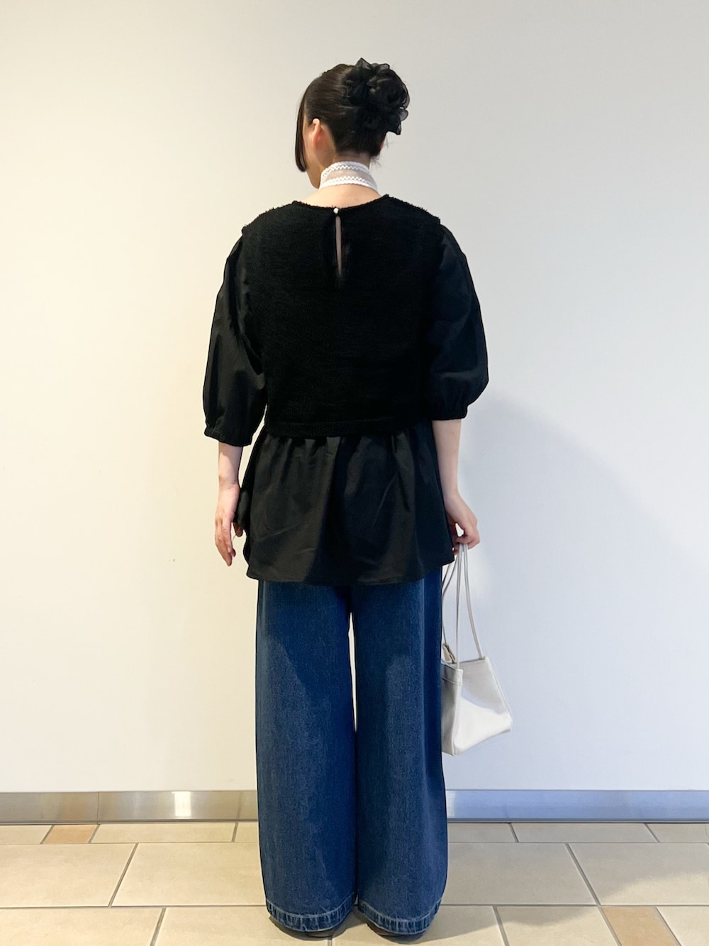 ブルー系のデニムパンツ、ブラック系のチュニック、ホワイト系のハンドバッグを着用したレディースの夏コーディネートの2枚目の写真