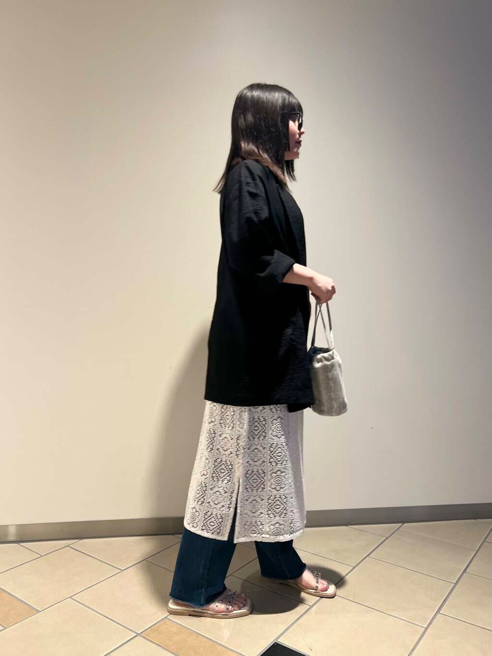 ホワイト系のハンドバッグ、ブラック系のテーラードジャケット、ホワイト系のサンダルを着用したレディースの夏コーディネートの3枚目の写真