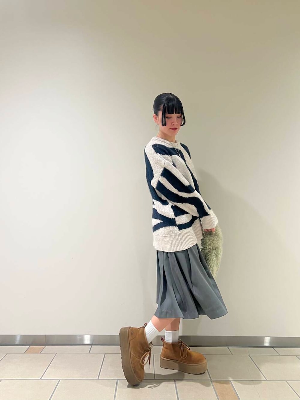 グレー系のスカート、グリーン系のハンドバッグ、ホワイト系のニット/セーターを着用したレディースの冬コーディネートの2枚目の写真