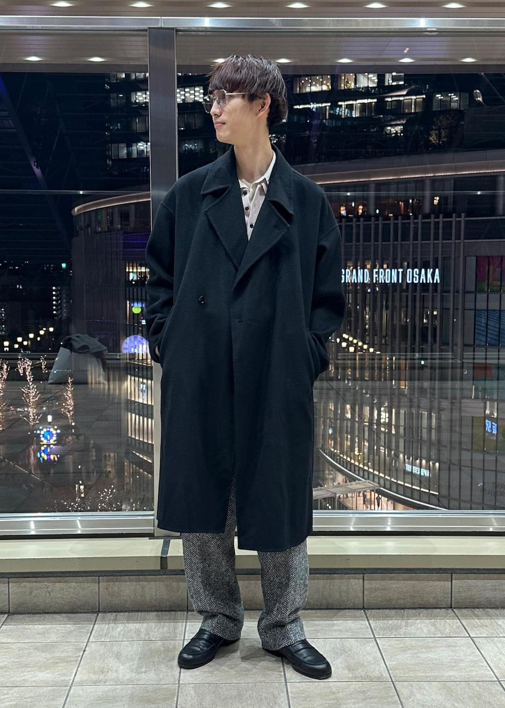 ブラック系のその他パンツ、ブラック系のステンカラーコート、ピンク系のポロシャツを着用したメンズの冬コーディネートの2枚目の写真