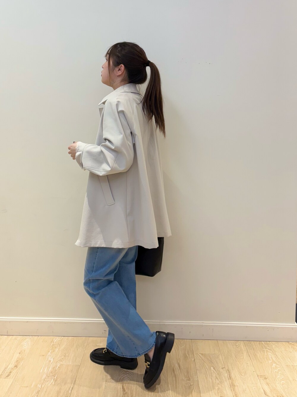 ブルー系のデニムパンツ、ブラック系のトートバッグ、ベージュ系のステンカラーコートを着用したレディースの冬コーディネートの3枚目の写真