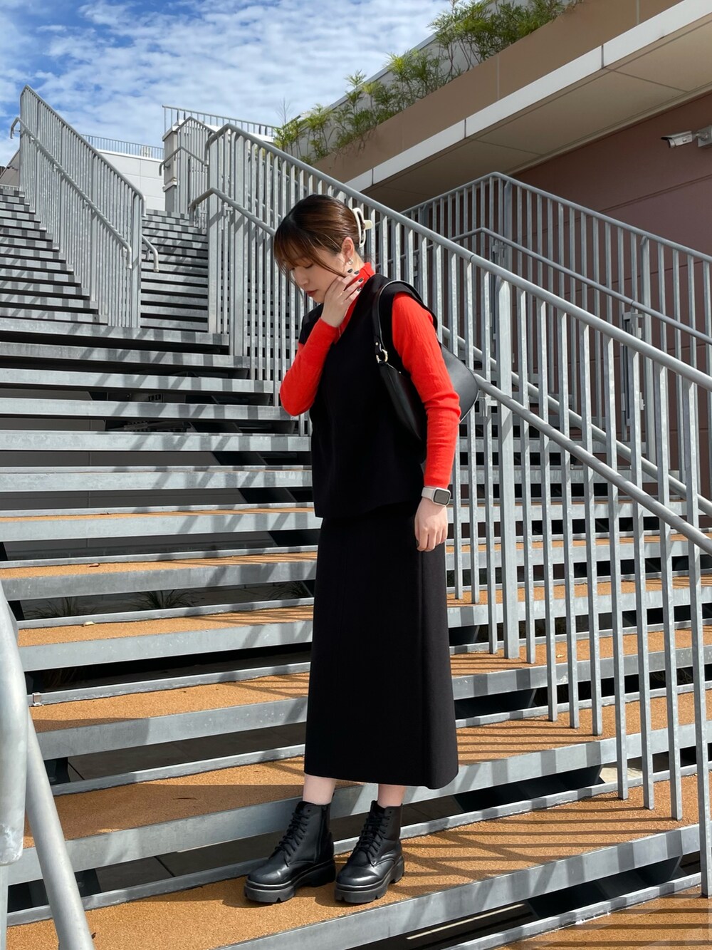 ブラック系のスカート、ブラック系のベスト、オレンジ系のニット/セーターを着用したレディースの秋コーディネートの5枚目の写真