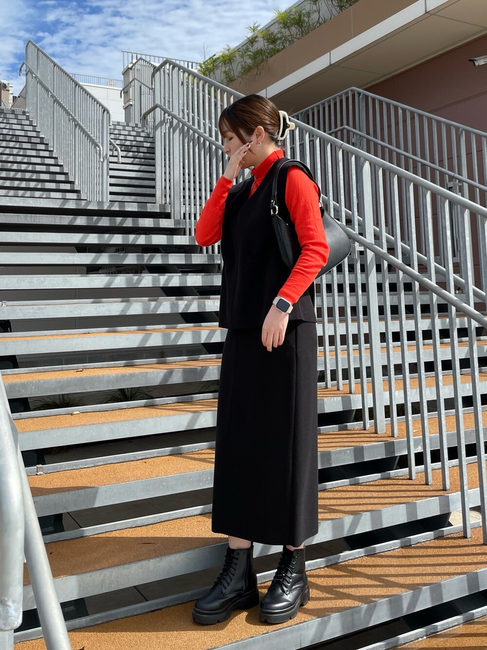 ブラック系のスカート、ブラック系のベスト、オレンジ系のニット/セーターを着用したレディースの秋コーディネートの3枚目の写真