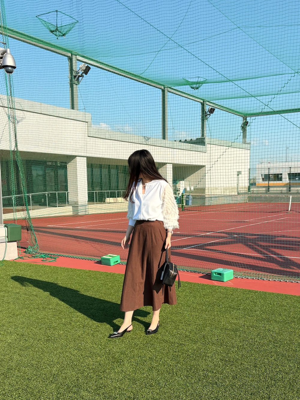 ブラック系のパンプス、ブラック系のショルダーバッグ、ブラウン系のスカートを着用したレディースの夏コーディネートの4枚目の写真