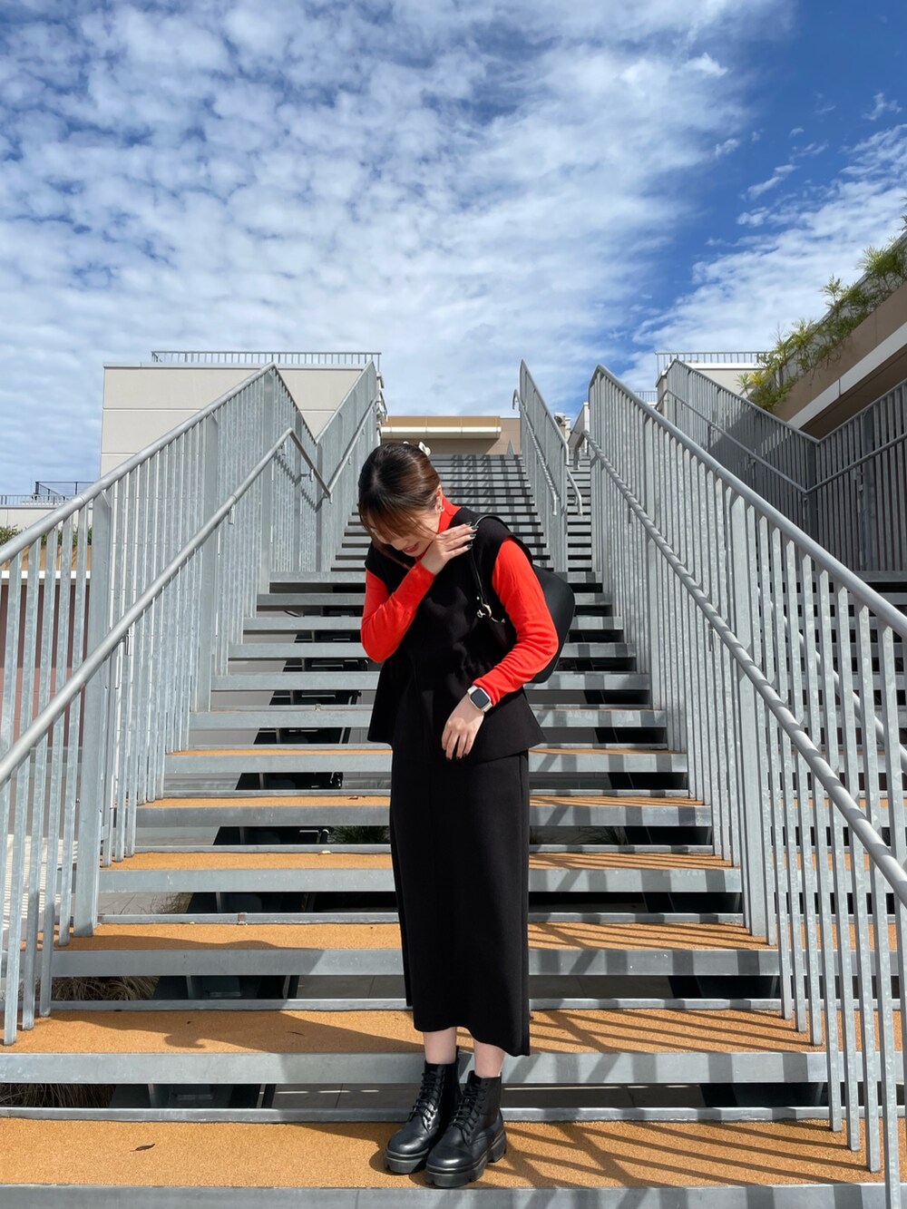 ブラック系のスカート、ブラック系のベスト、オレンジ系のニット/セーターを着用したレディースの秋コーディネートの2枚目の写真