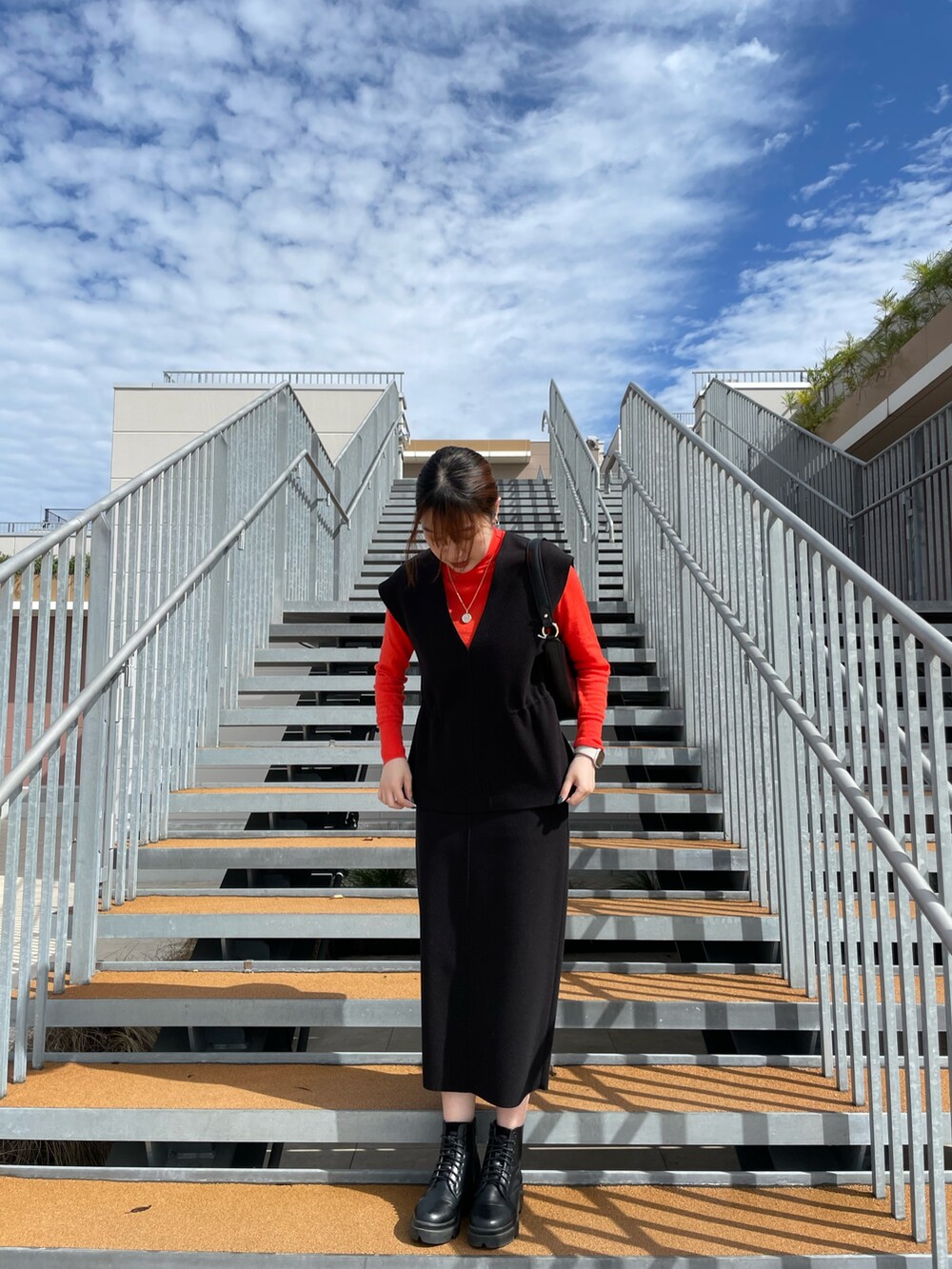 ブラック系のスカート、ブラック系のベスト、オレンジ系のニット/セーターを着用したレディースの秋コーディネートの4枚目の写真