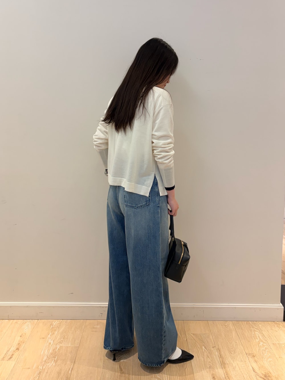 ブラック系のショルダーバッグ、ブルー系のデニムパンツ、ホワイト系のニット/セーターを着用したレディースの秋コーディネートの2枚目の写真