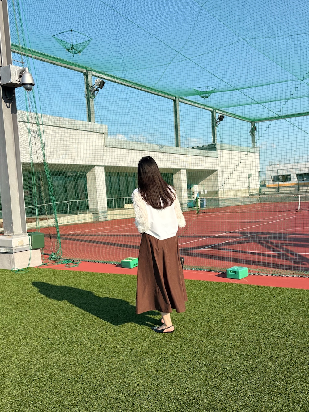 ブラック系のパンプス、ブラック系のショルダーバッグ、ブラウン系のスカートを着用したレディースの夏コーディネートの2枚目の写真