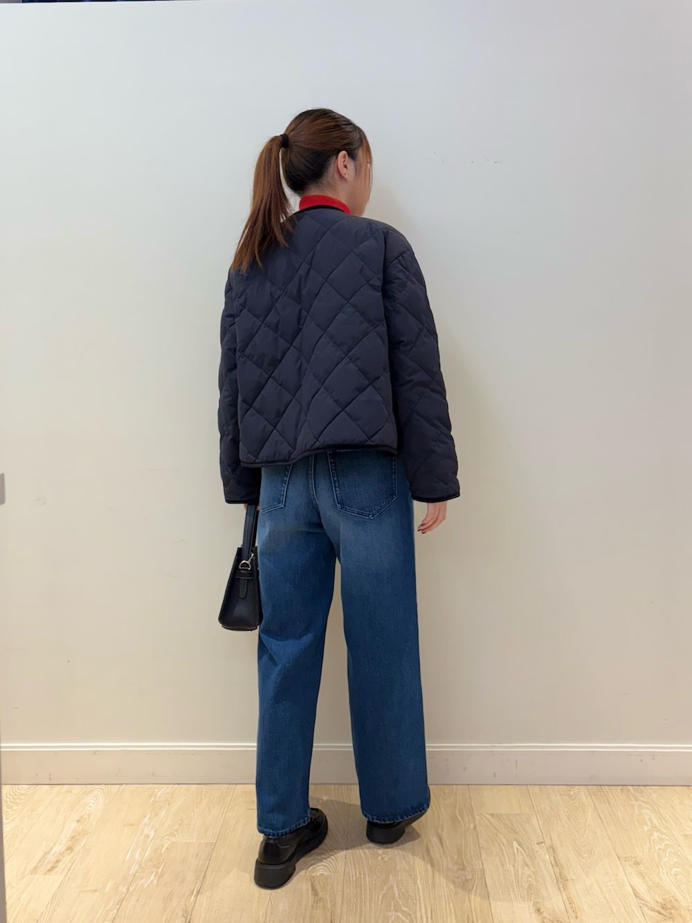 ブルー系のデニムパンツ、ブラック系のショルダーバッグ、レッド系のニット/セーターを着用したレディースの秋コーディネートの3枚目の写真