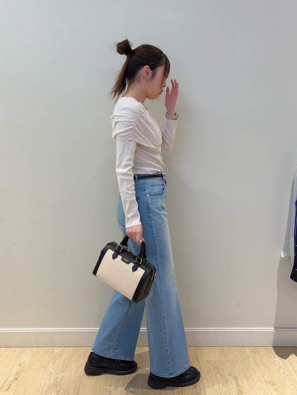 ブラック系のボストンバッグ、ブルー系のデニムパンツ、ベージュ系のニット/セーターを着用したレディースの春コーディネートの3枚目の写真