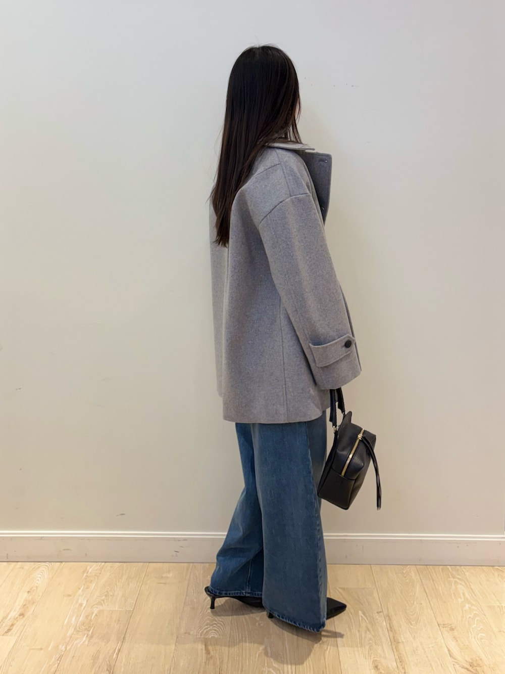 ブラック系のショルダーバッグ、ブルー系のデニムパンツ、グレー系のピーコートを着用したレディースの秋コーディネートの3枚目の写真
