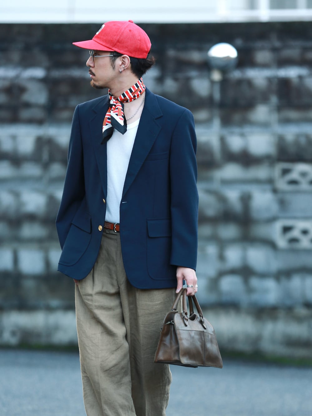 ブラウン系のハンドバッグ、ブラック系のドレスシューズ、レッド系のキャップを着用したメンズの秋コーディネートの2枚目の写真