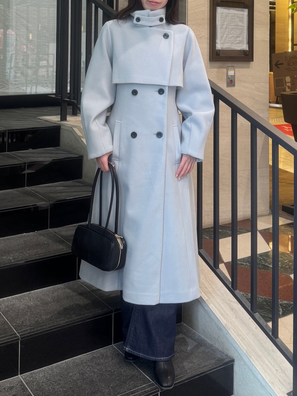 グレー系のトレンチコート、ブルー系のデニムパンツ、ブラック系のブーツを着用したレディースの秋コーディネートの2枚目の写真