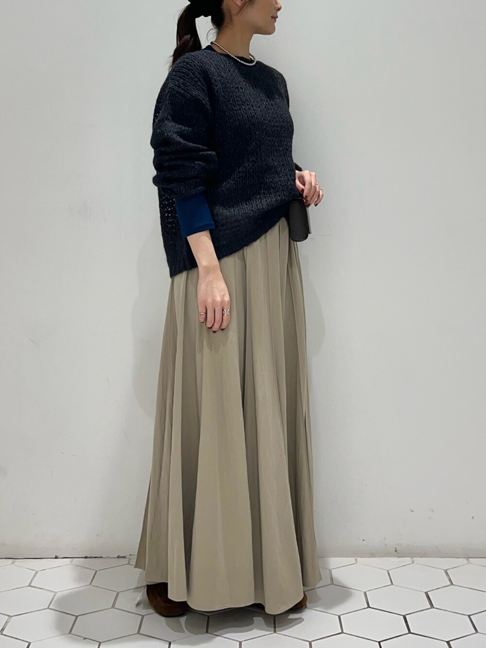 グレー系のニット/セーター、ブルー系のTシャツ/カットソー、ベージュ系のスカートを着用したレディースの秋コーディネートの4枚目の写真