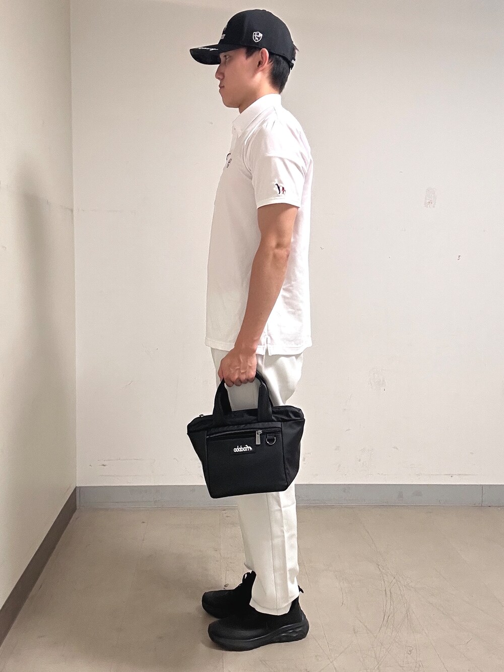 ホワイト系のポロシャツ、グレー系のその他パンツ、ブラック系のキャップを着用したメンズの夏コーディネートの2枚目の写真