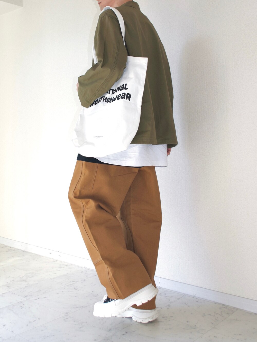 ホワイト系のTシャツ/カットソー、ブラウン系のチノパンツ、ホワイト系のトートバッグを着用したメンズの秋コーディネートの2枚目の写真