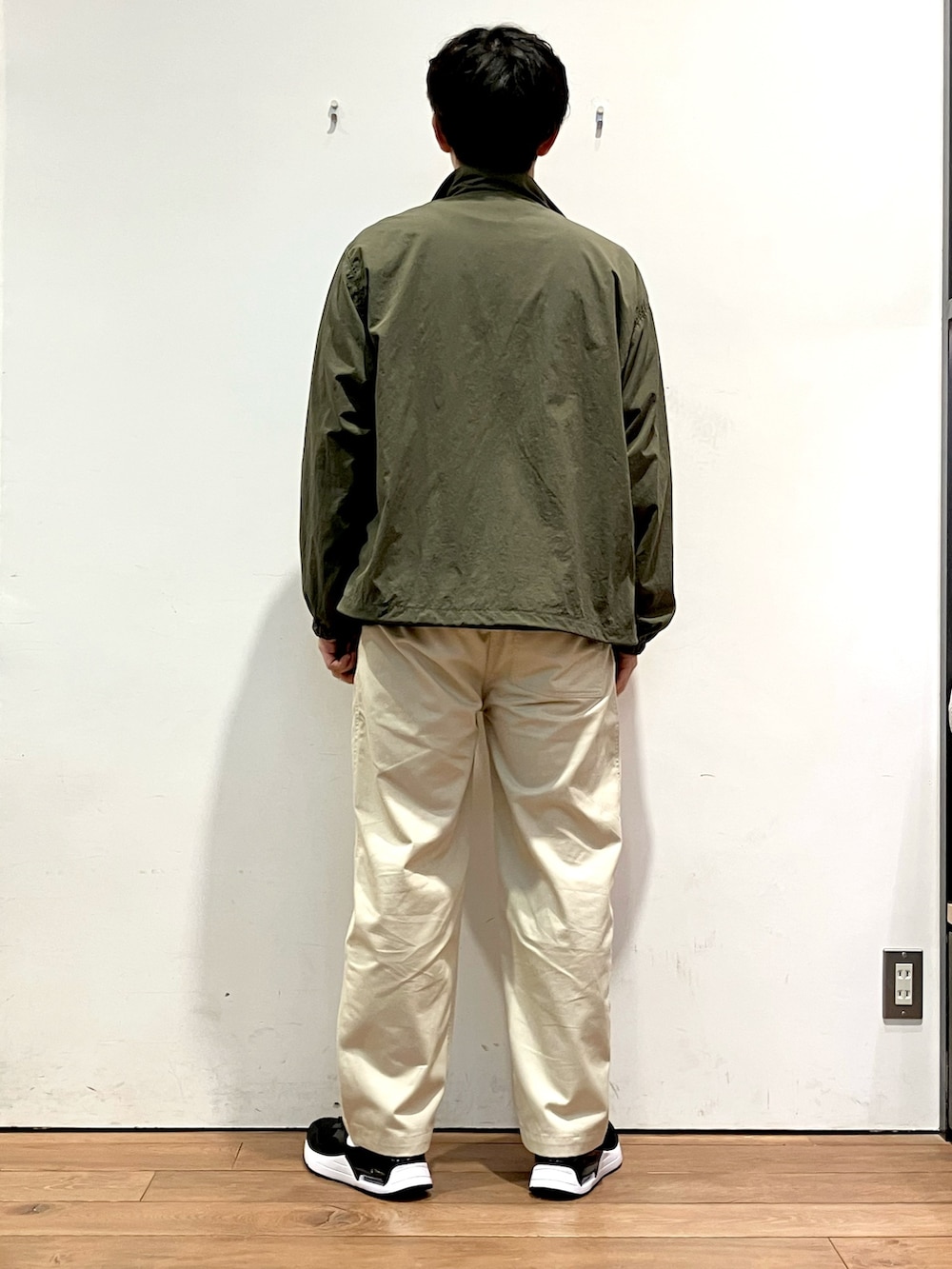 グリーン系のナイロンジャケット、ブルー系のニット/セーター、ホワイト系のチノパンツを着用したメンズの秋コーディネートの3枚目の写真