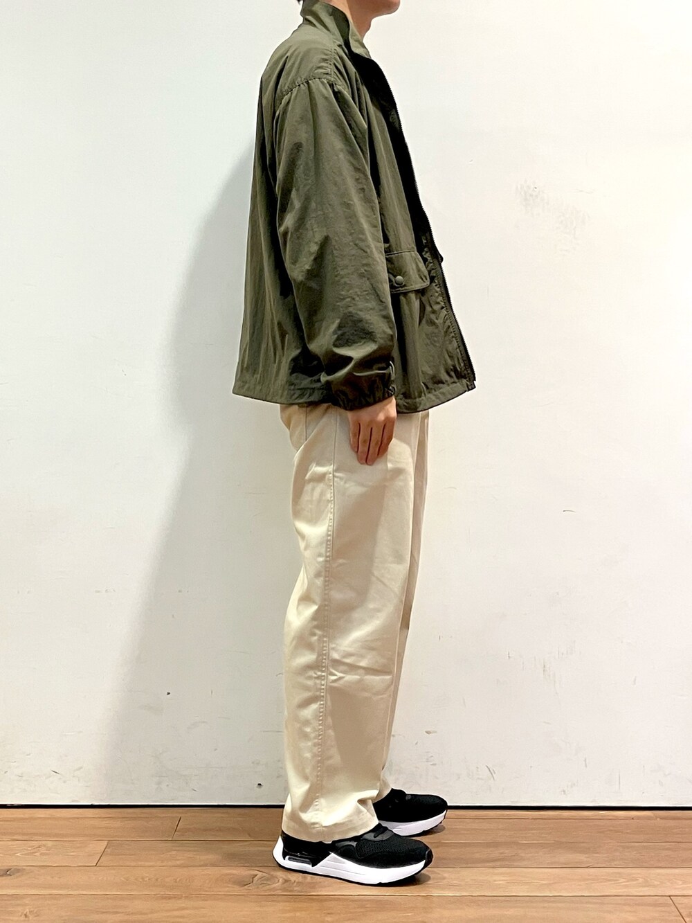 グリーン系のナイロンジャケット、ブルー系のニット/セーター、ホワイト系のチノパンツを着用したメンズの秋コーディネートの2枚目の写真