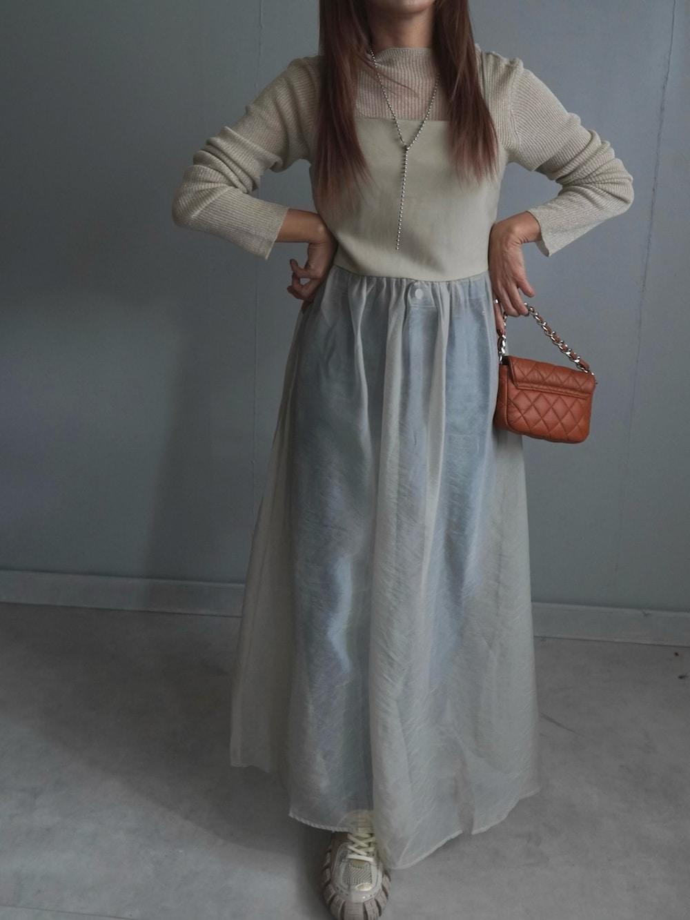 ベージュ系のワンピース、ブルー系のデニムパンツ、ブラウン系のトップスを着用したレディースの春コーディネートの2枚目の写真