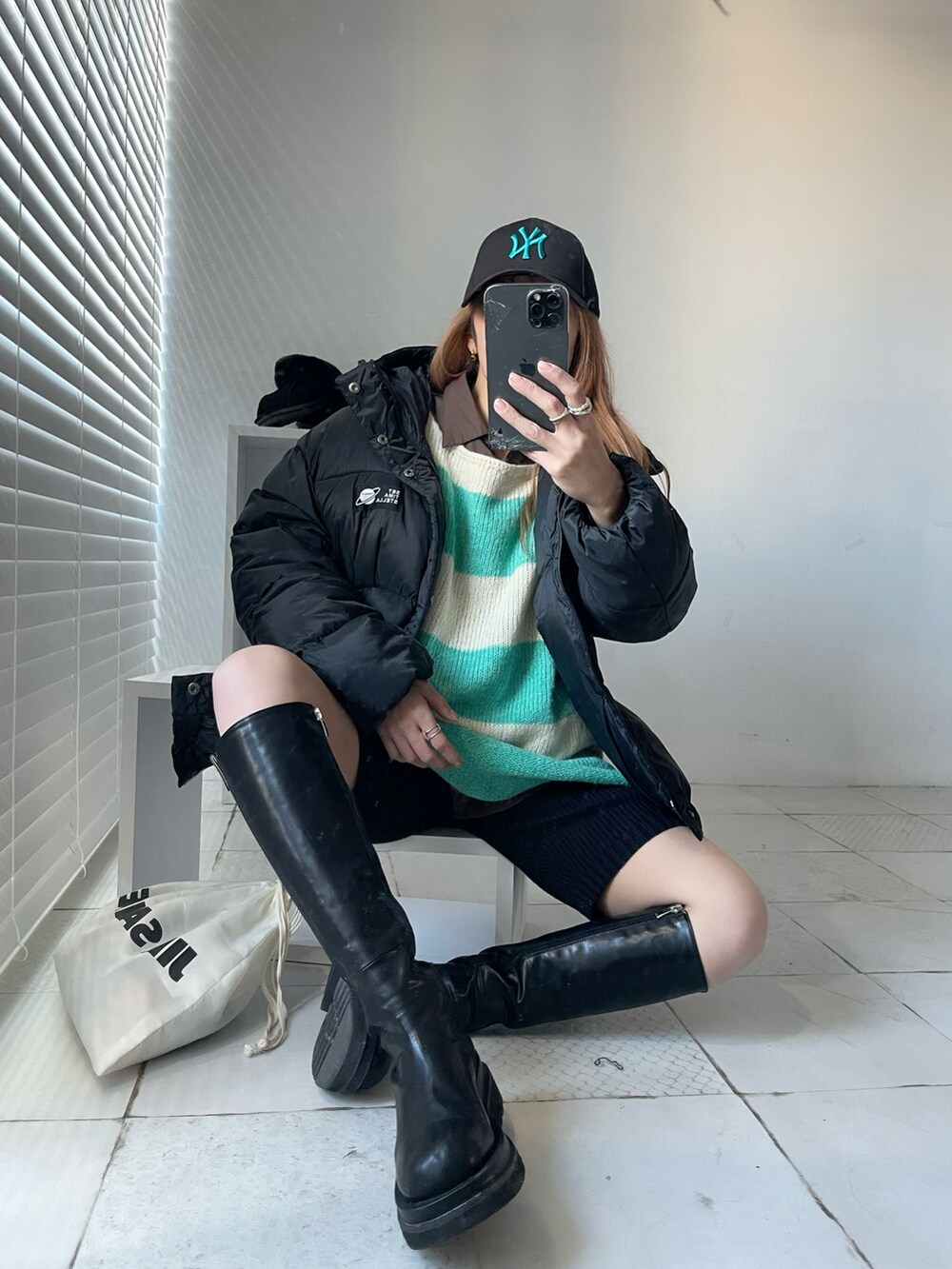 グリーン系のニット/セーター、ブラック系のブーツ、ホワイト系のショルダーバッグを着用したレディースの秋コーディネートの5枚目の写真