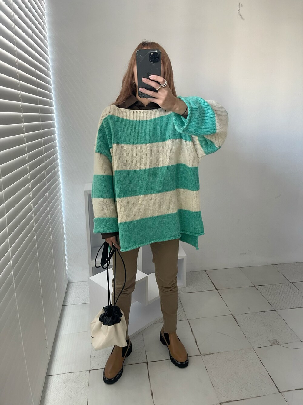 グリーン系のニット/セーター、ブラック系のブーツ、ホワイト系のショルダーバッグを着用したレディースの秋コーディネートの4枚目の写真