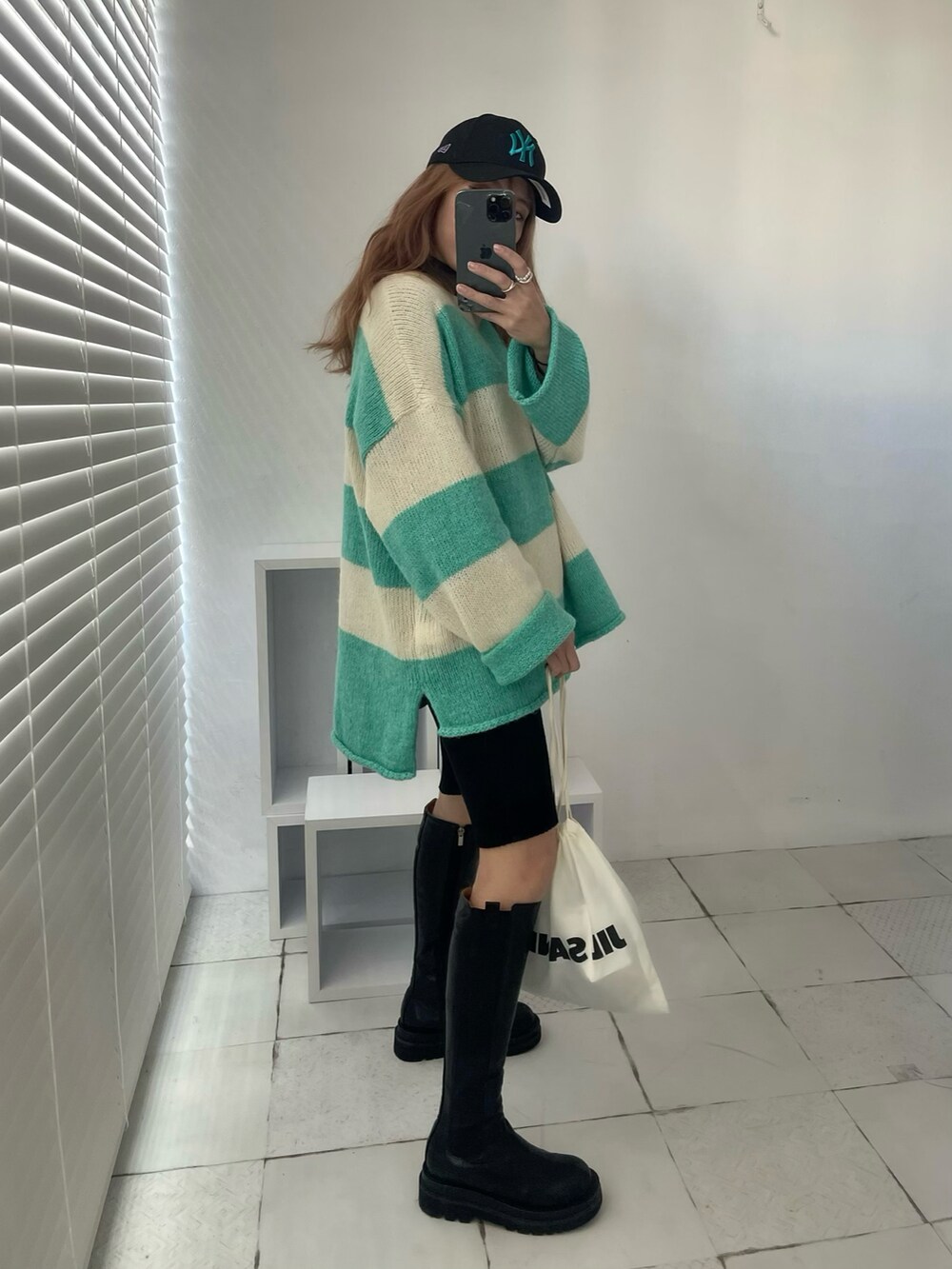 グリーン系のニット/セーター、ブラック系のブーツ、ホワイト系のショルダーバッグを着用したレディースの秋コーディネートの3枚目の写真