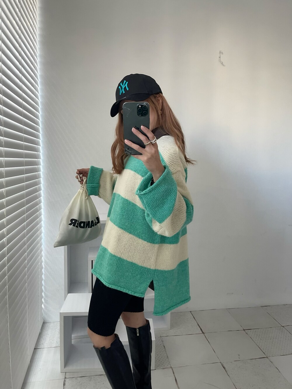 グリーン系のニット/セーター、ブラック系のブーツ、ホワイト系のショルダーバッグを着用したレディースの秋コーディネートの2枚目の写真