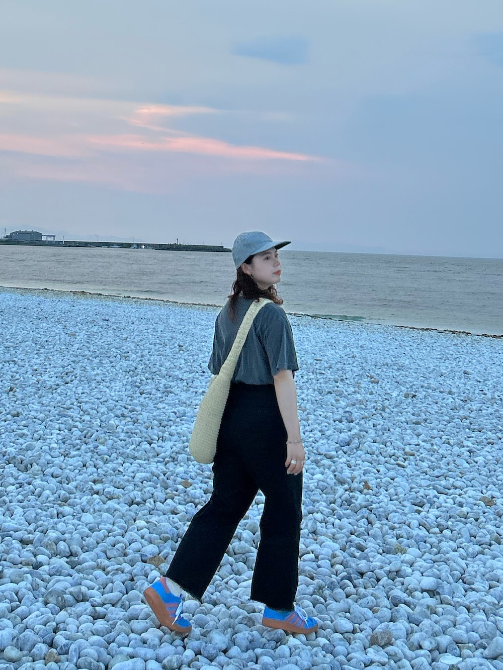 ベージュ系のショルダーバッグ、ブラック系のチノパンツ、ブルー系のスニーカーを着用したレディースの夏コーディネートの2枚目の写真