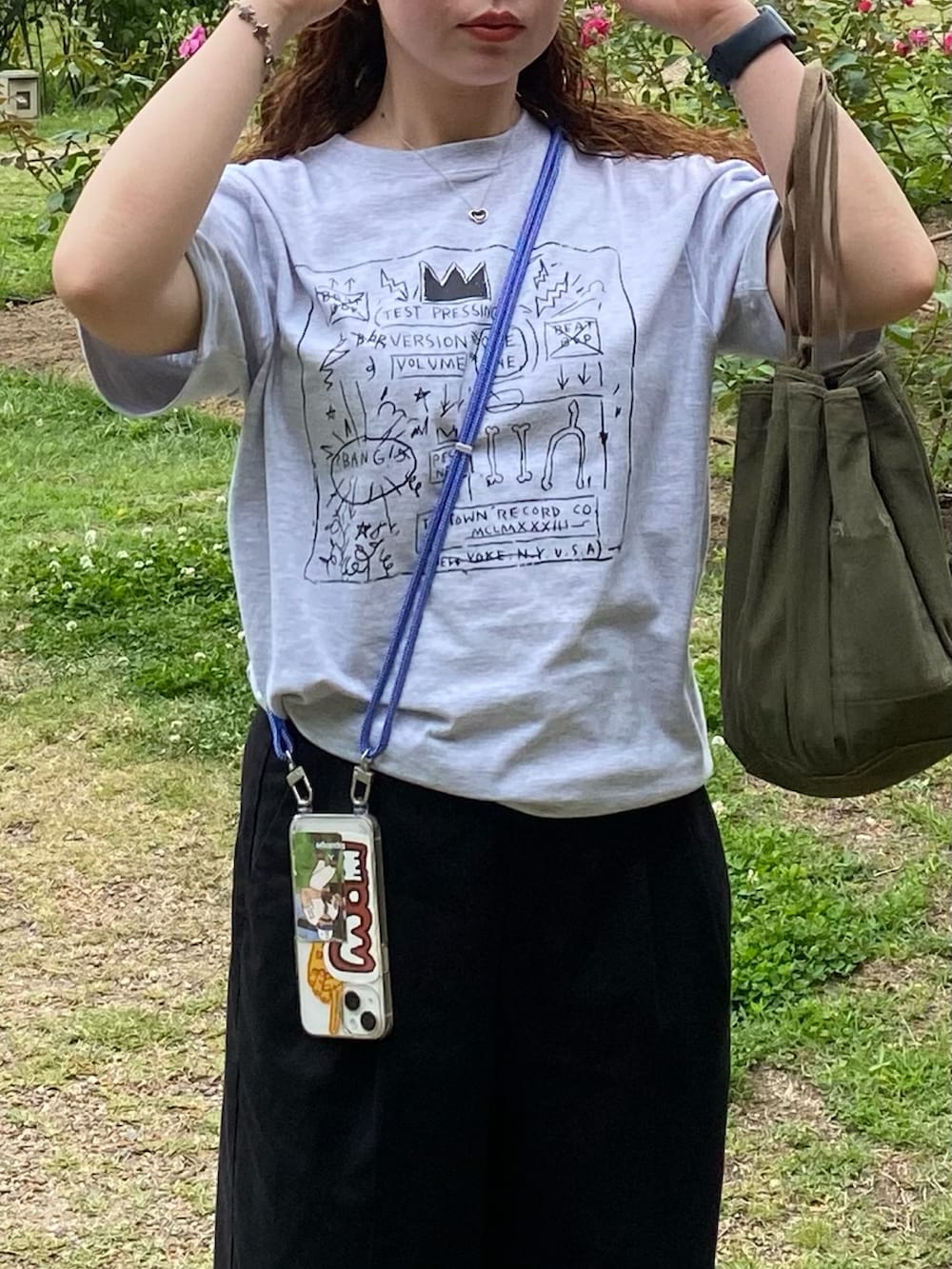 グレー系のTシャツ/カットソー、グリーン系のハンドバッグ、ブラック系のスラックスを着用したレディースの夏コーディネートの2枚目の写真