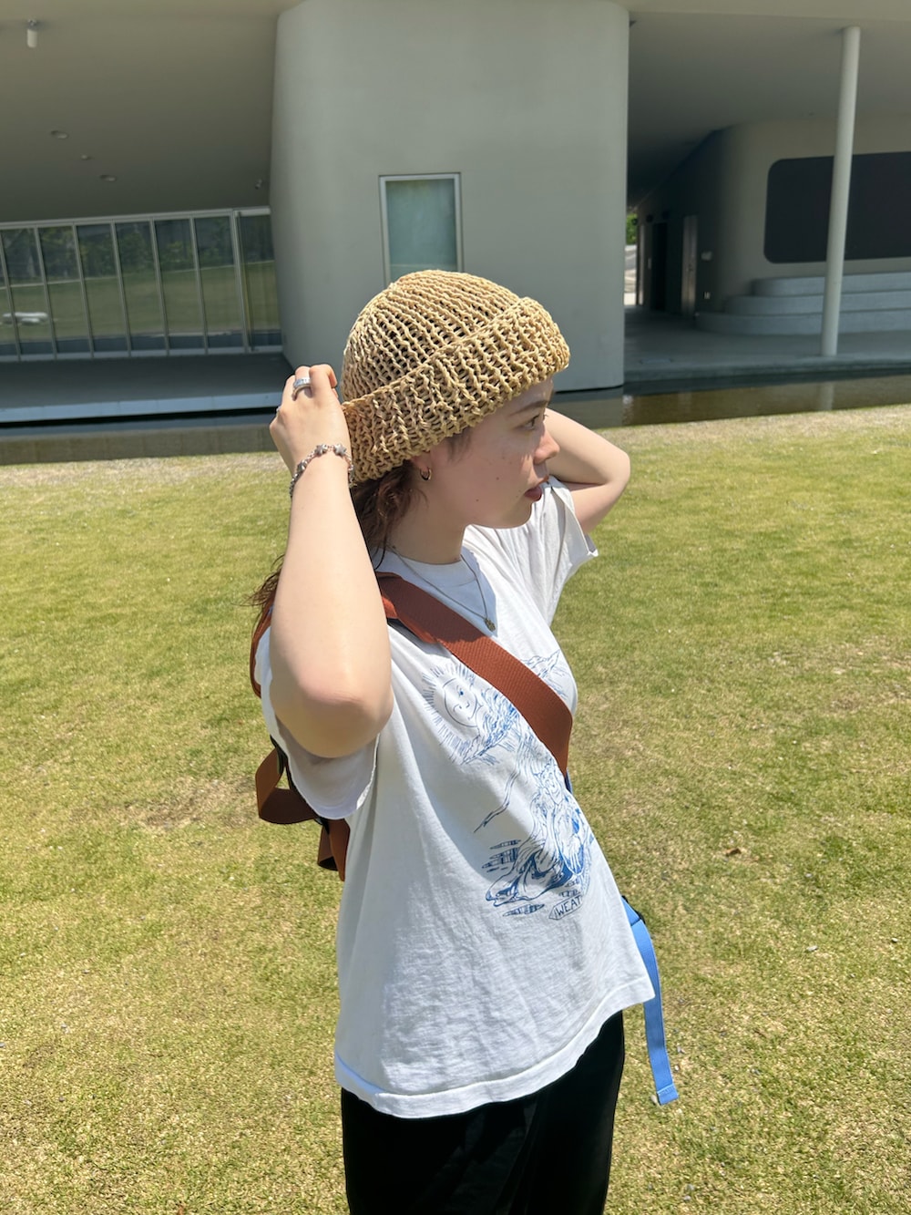 ブラック系のスラックス、ブラウン系のスニーカー、オレンジ系のメッセンジャーバッグを着用したレディースの夏コーディネートの3枚目の写真